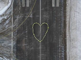 Aerial view of a runway with a large heart shape created using yellow paint or material in the center. The surrounding area includes textured surfaces with shades of gray and hints of snow or ice along the edges.
