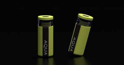 Two yellow cylindrical water bottles with black lids and vertical black stripes featuring the word 'AQUA' are placed against a dark background. One bottle stands upright while the other is slightly tilted.