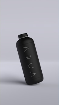 A sleek matte black bottle with minimalistic design, featuring the word 'AQUA' written vertically. The bottle is slightly tilted against a muted gray background.