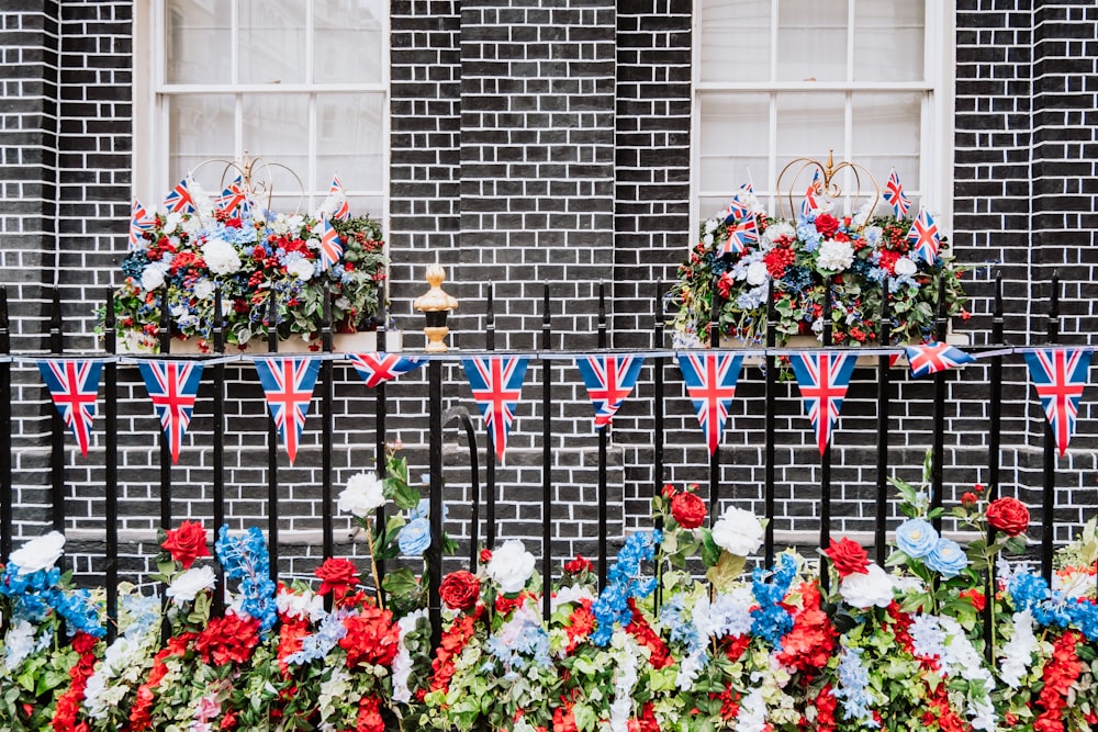 a fence with flowers and flags on it in front of a building