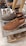 A pair of casual lace-up shoes displayed on a glass shelf in a shoe store. One shoe is brown and the other is dark brown, showcasing a textured material. In the background, additional pairs of shoes are visible, including slip-ons and loafers, all arranged neatly on shelves.