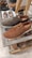 A pair of casual lace-up shoes displayed on a glass shelf in a shoe store. One shoe is brown and the other is dark brown, showcasing a textured material. In the background, additional pairs of shoes are visible, including slip-ons and loafers, all arranged neatly on shelves.