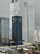 Several high-rise buildings are in an urban area with overcast skies. Prominent skyscrapers feature glass facades and modern architecture, including a building with a visible 'Westin' logo. The foreground shows a rooftop landscape with residential structures and greenery.