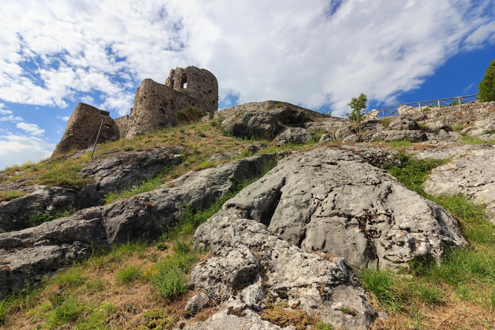 a rocky hillside with grass and rocks under a cloudy blue sky