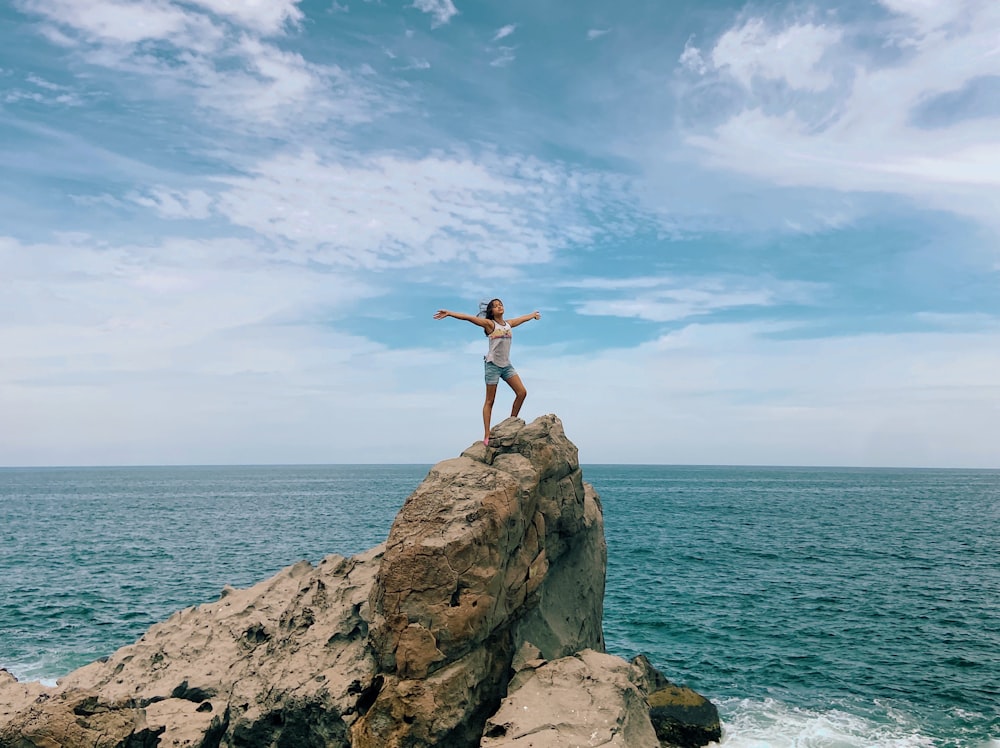 a woman standing on top of a rock near the ocean
