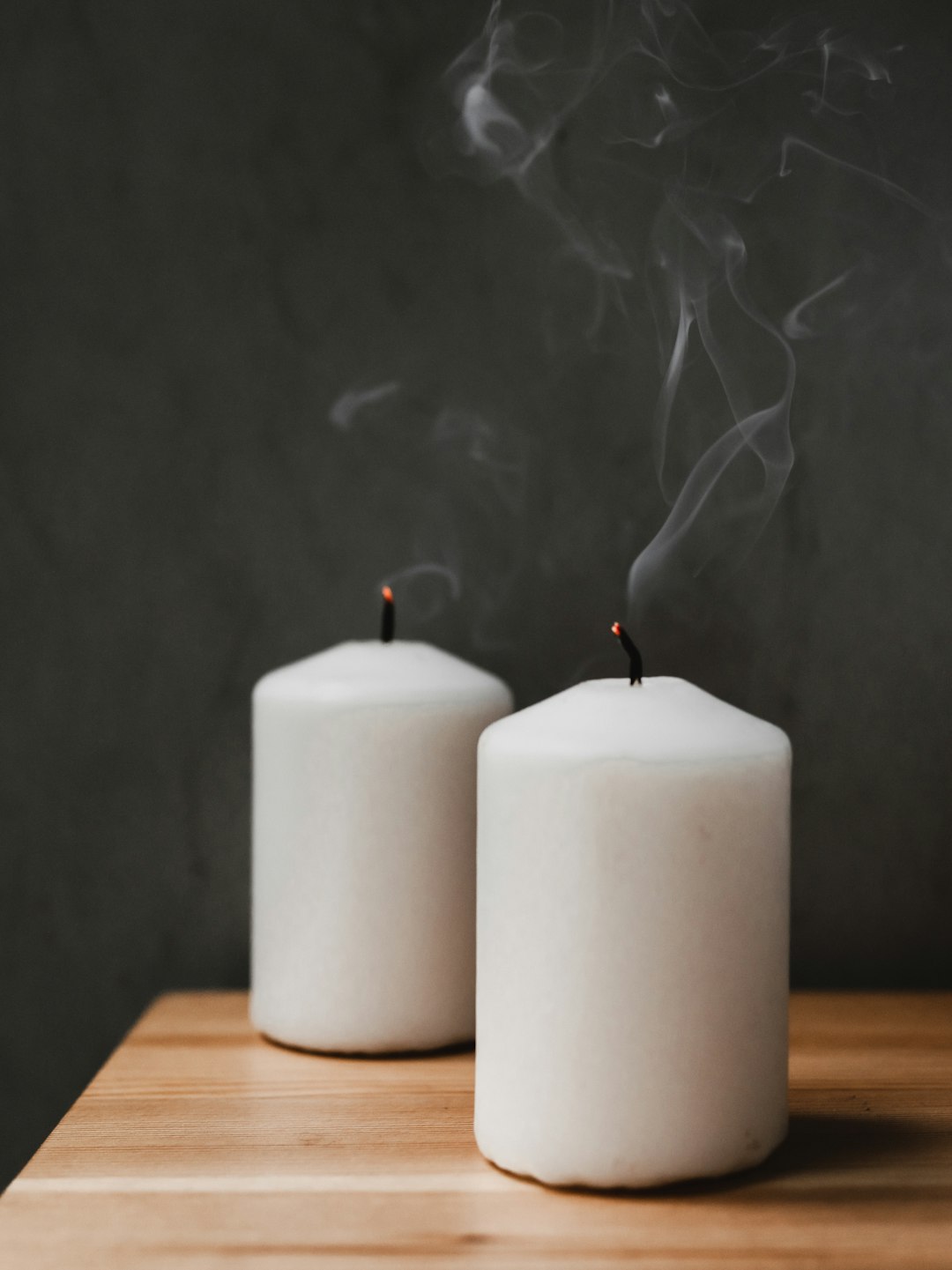 a couple of white candles sitting on top of a wooden table