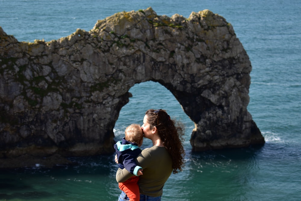 a woman holding a child while standing next to a body of water