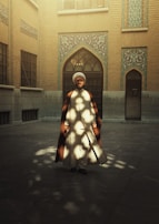 A serene portrait of a man in a flowing black jubba standing in a sunlit courtyard.
