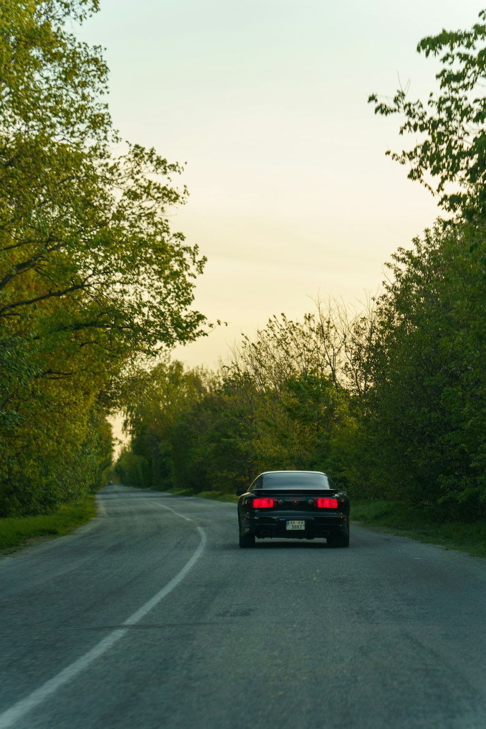a black car driving down a tree lined road