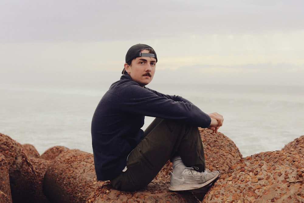 a man sitting on top of a rock near the ocean