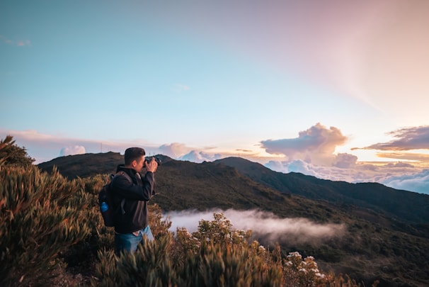 A candid photo of a backpacker standing on a mountain ridge overlooking a misty Asian valley at sunrise.