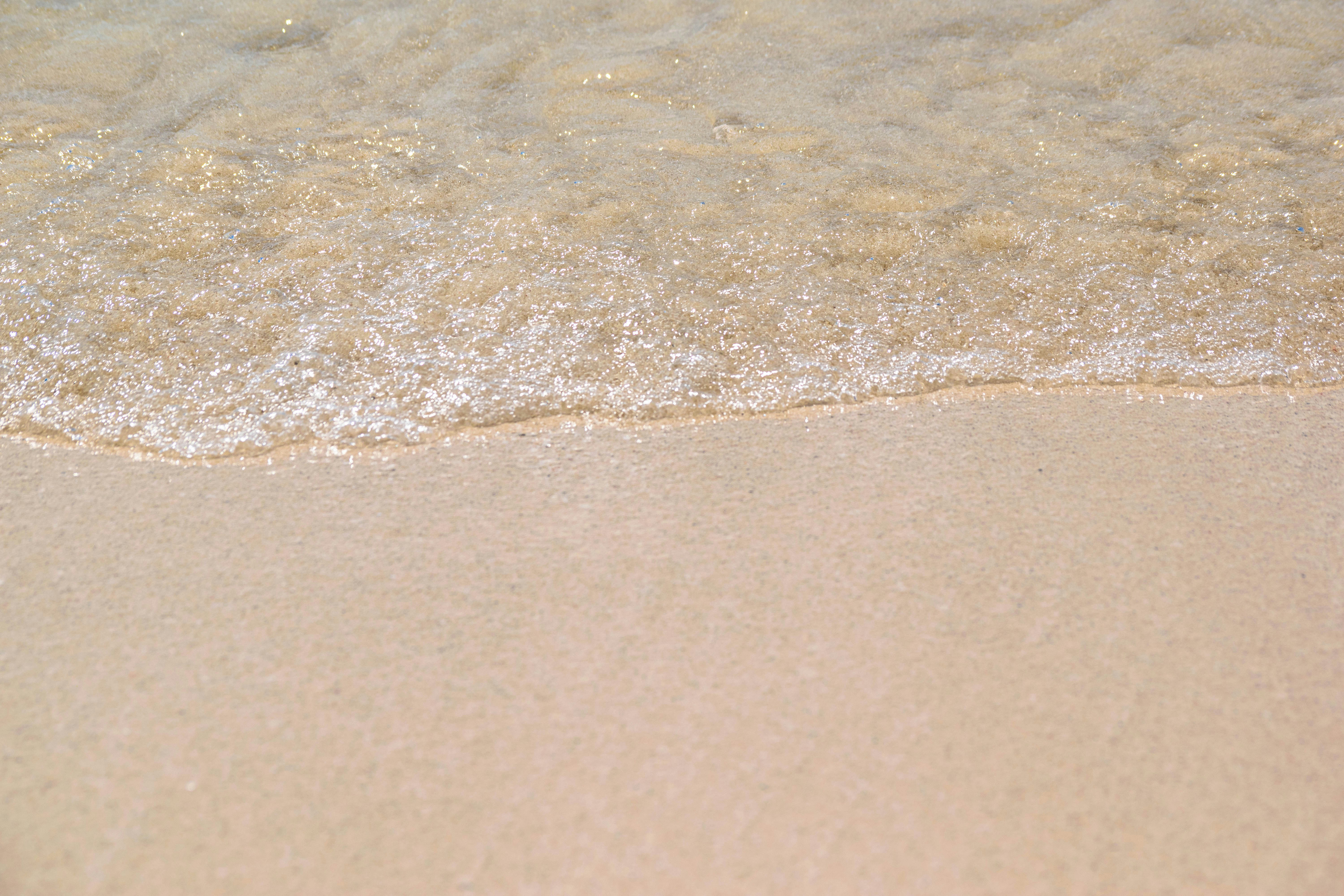 a close up of the sand and water of a beach, The sand in Cancun is white because it is composed of pieces of coral defecated by the Parrotfish, which is mostly found in the area. The white color of the sand also helps keep it cool by reflecting the sun