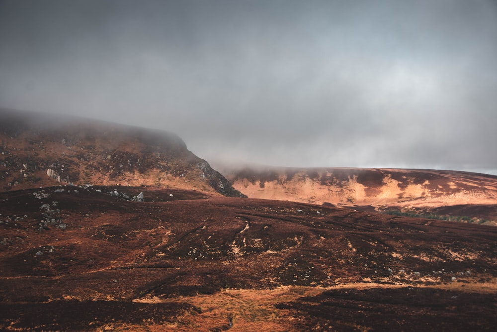 a hill covered in brown grass under a cloudy sky