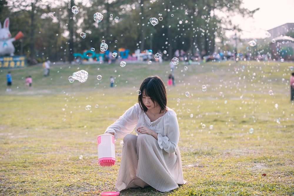a woman sitting on the ground blowing bubbles