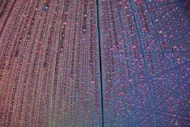 A mesmerizing display of multicolored lights creating a starry, cosmic effect. Strings of tiny, vibrant lights hang vertically, casting a magical and immersive atmosphere. The lights reflect and shimmer in various colors, including pink, blue, green, and purple, forming a dynamic and enchanting visual spectacle.
