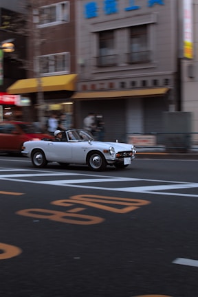 White luxury convertible cruising through a city street with skyscrapers.