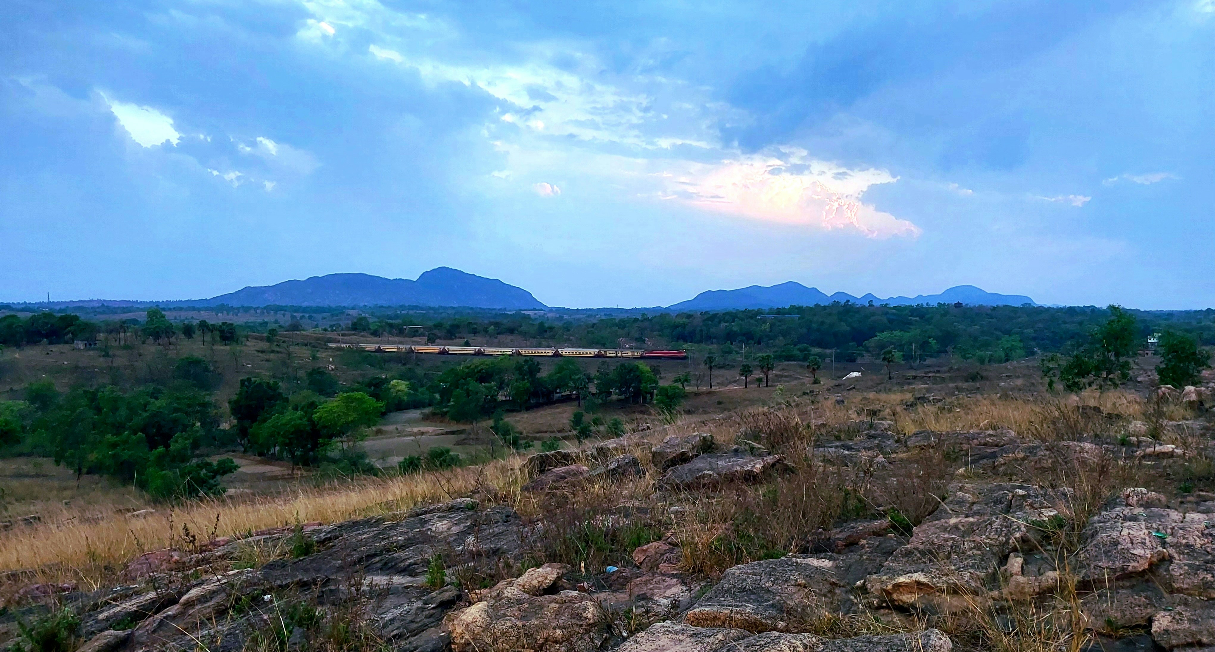 a field with rocks and grass and mountains in the background