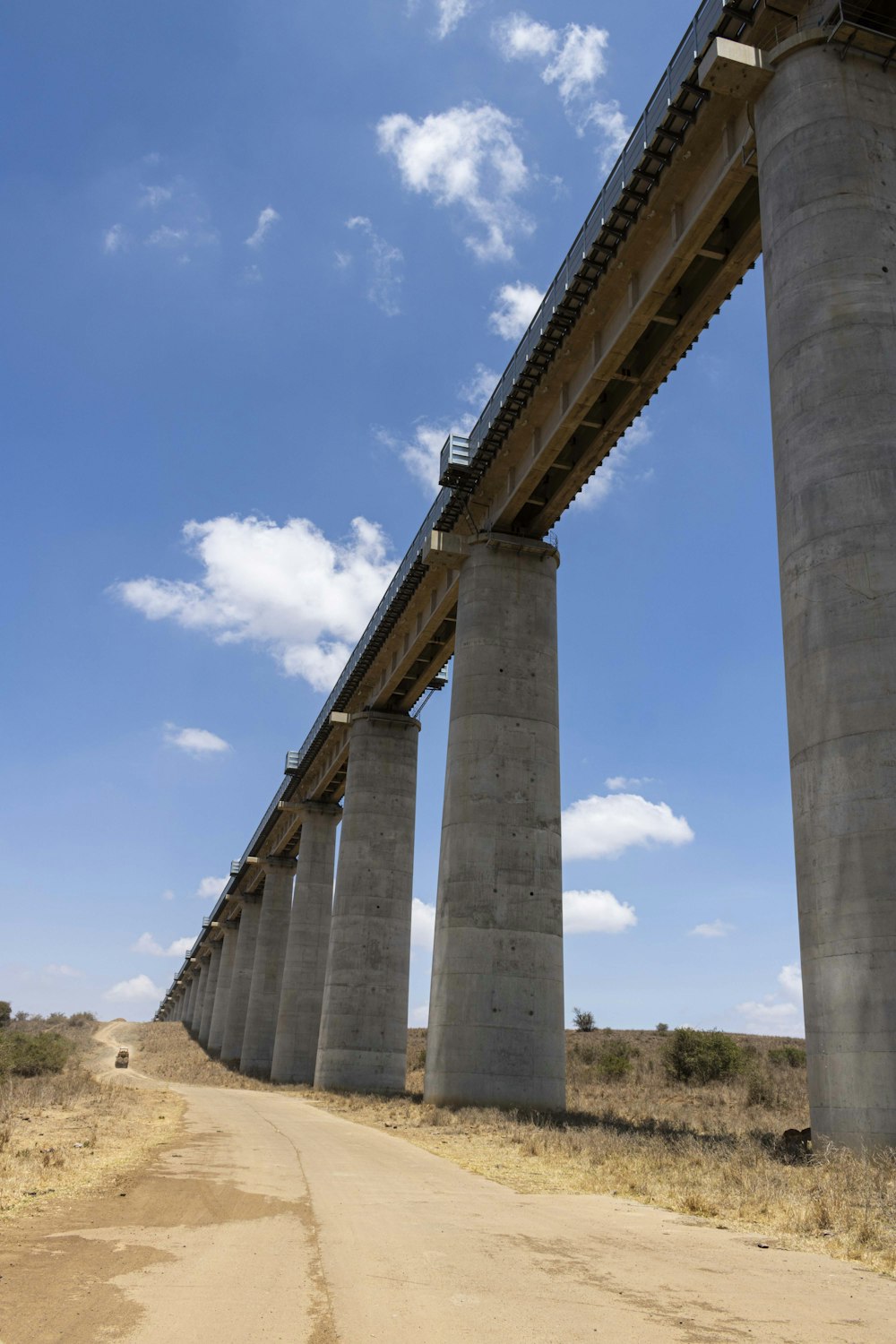 a long bridge over a dirt road under a blue sky