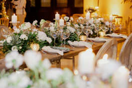 A warmly lit reception table set with candles, floral centerpieces, and personalized place cards.