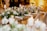 An elegantly set table with white floral arrangements and greenery cascading down the center. The table is adorned with candles and sparkling glassware, creating a warm and inviting atmosphere. The soft lighting enhances the overall sophisticated ambience.