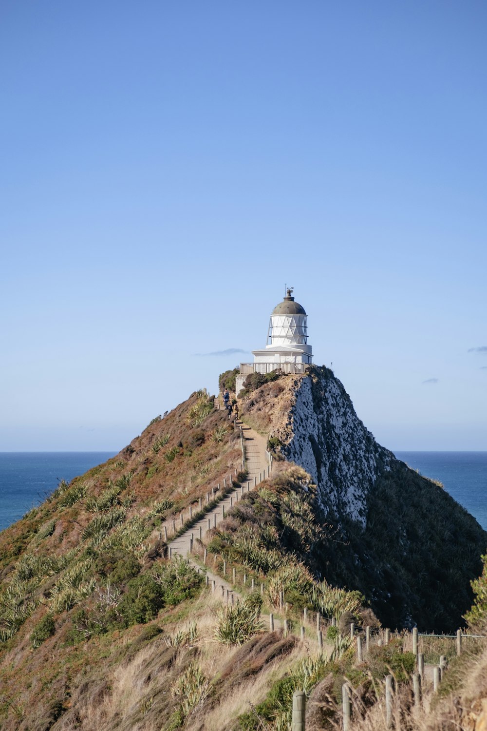 a white lighthouse on top of a hill next to the ocean