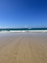 A peaceful beach scene with soft white sand and gentle waves under a clear blue sky.