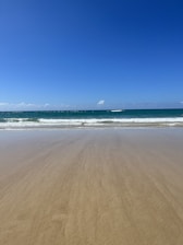 A serene beach view showcasing soft sands and gentle waves under a clear blue sky.