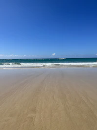 A serene beach scene with golden sand and calm blue waves under a clear sky.