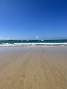 A serene beach scene with golden sand and calm blue waves under a clear sky.