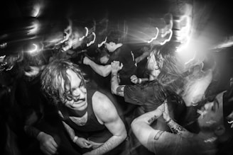 A dynamic black-and-white shot of a live concert crowd, captured with smooth slow-motion drone footage under moody lighting.