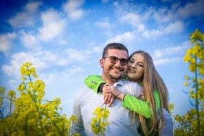 A smiling couple capturing memories against a vibrant summer-themed wall with bright sunflowers and blue skies.
