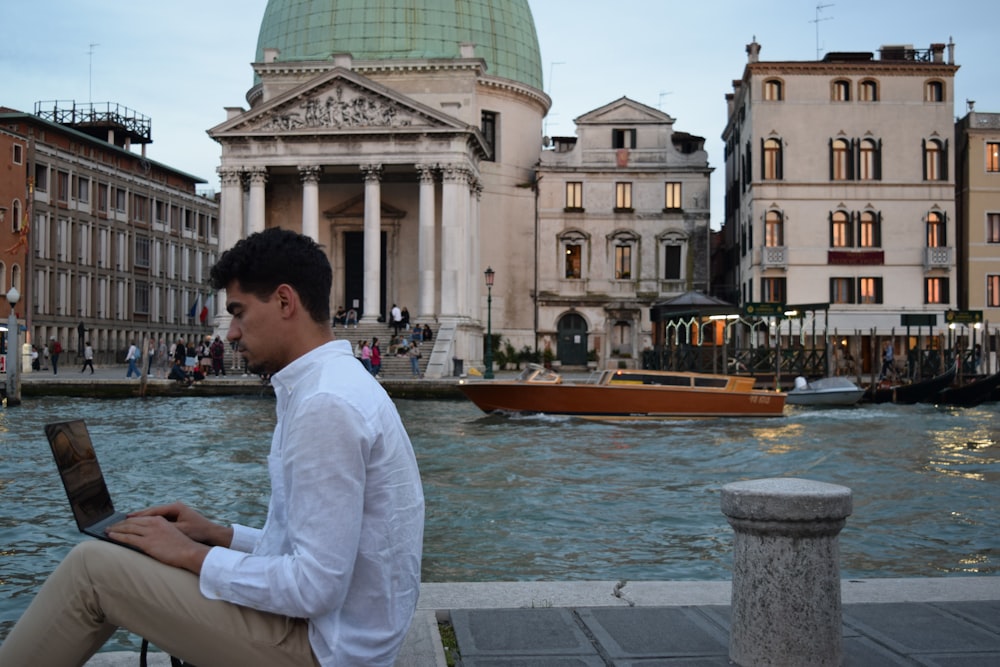 a man sitting on a ledge using a laptop