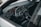 A sleek car interior featuring a leather-wrapped steering wheel with the Volkswagen logo, surrounded by a modern dashboard with digital displays and various controls. The layout includes air vents, an infotainment system, and a gear shift. The color scheme is predominantly dark with metallic accents.