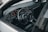 A sleek car interior featuring a leather-wrapped steering wheel with the Volkswagen logo, surrounded by a modern dashboard with digital displays and various controls. The layout includes air vents, an infotainment system, and a gear shift. The color scheme is predominantly dark with metallic accents.