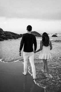 A romantic couple walking hand in hand on the shore.