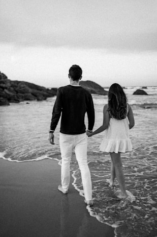A romantic couple walking hand in hand on the shore.