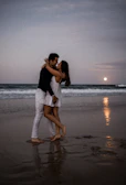 A couple enjoying a romantic dinner on the beach with soft candlelight and gentle waves nearby.