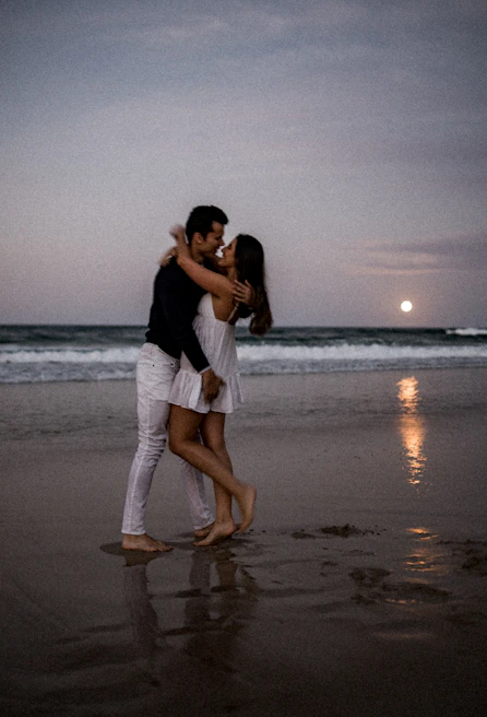 Two avatars sharing a close embrace on a moonlit virtual beach with gentle waves.