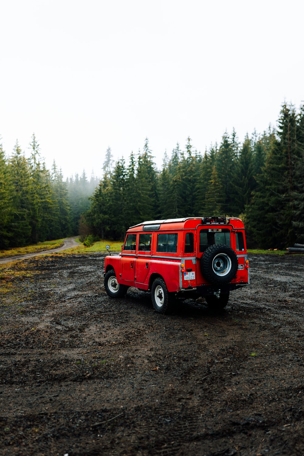 a red jeep is parked on a dirt road