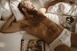 a shirtless man laying in bed next to a book