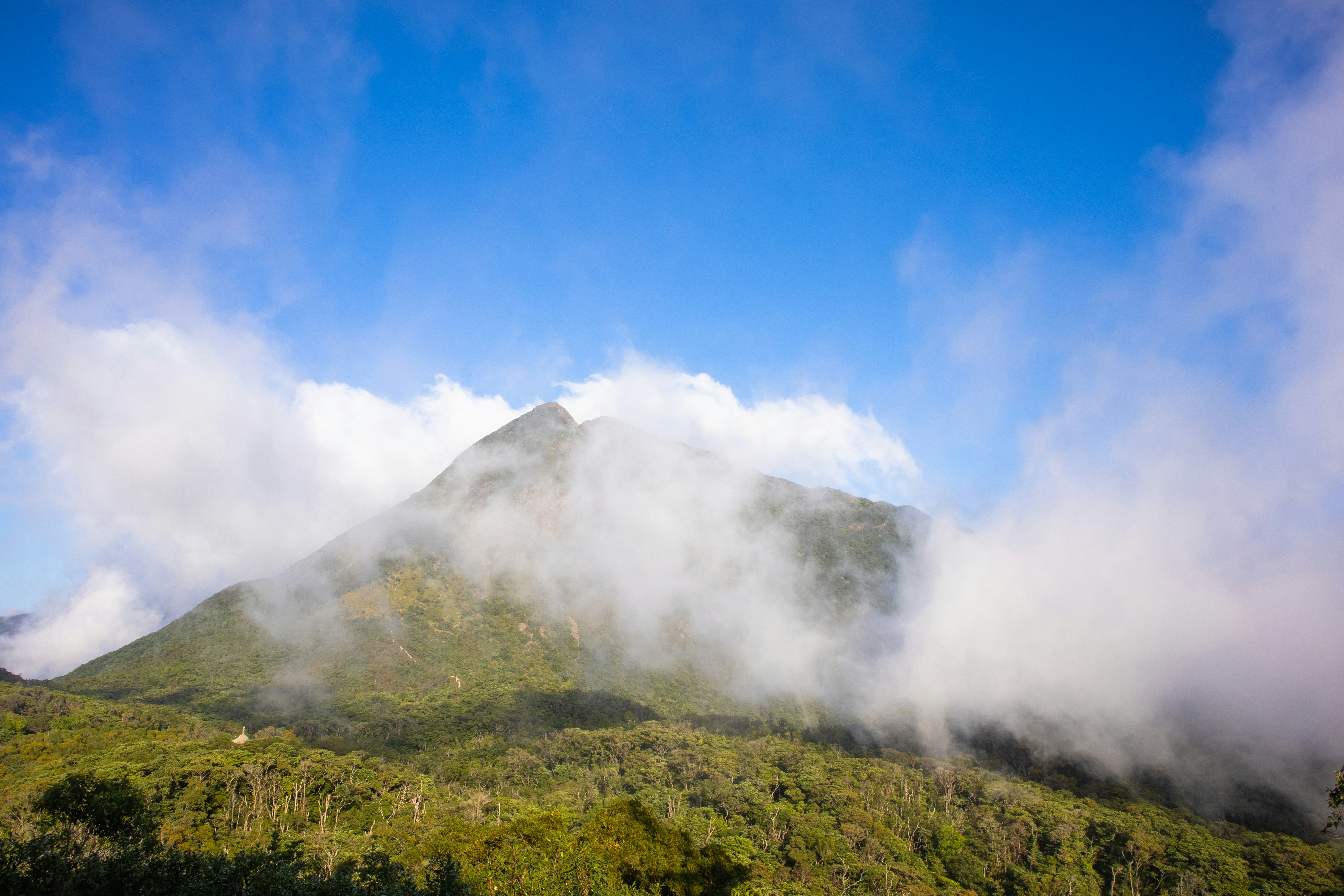 a mountain covered in mist and clouds on a sunny day