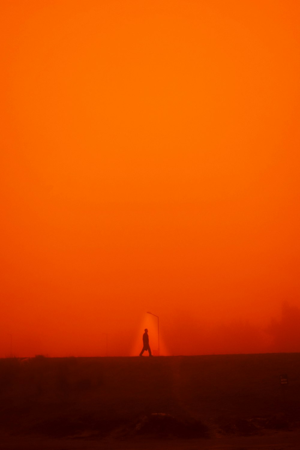 a person walking across a field under an orange sky