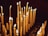 Numerous tall, wax candles are lit and arranged in rows, with soft, warm flames flickering in a dimly lit environment. Some candles are burned down more than others, and melted wax has dripped onto the surface below.