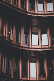 Curved sections of a modern building facade with large glass windows framed by bronze or dark metallic panels, creating a sleek and urban architectural appearance.