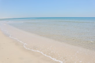 Crystal-clear ocean waves gently lapping against a pristine white sandy beach under a bright blue sky.