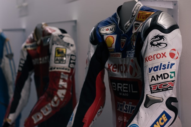 A sleek black and red F1 racing jacket displayed on a mannequin with a blurred racetrack background.