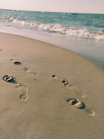Footprints in the sand along a serene beach at sunset, inviting a peaceful walk.