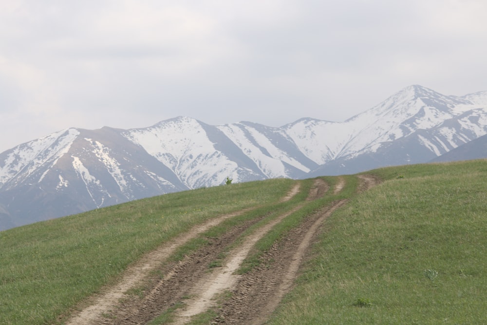 a dirt road on a grassy hill with mountains in the background