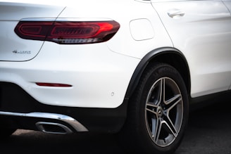 A close-up rear view of a white Mercedes-Benz SUV, focusing on the tail light, rear tire, and part of the bumper. The 4MATIC badge is visible, along with the Michelin branding on the tire.