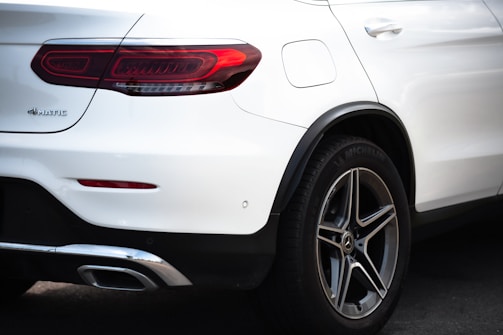 A close-up rear view of a white Mercedes-Benz SUV, focusing on the tail light, rear tire, and part of the bumper. The 4MATIC badge is visible, along with the Michelin branding on the tire.